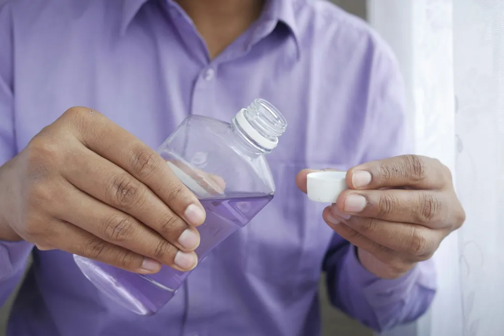 Person in purple shirt holding mouthwash bottle