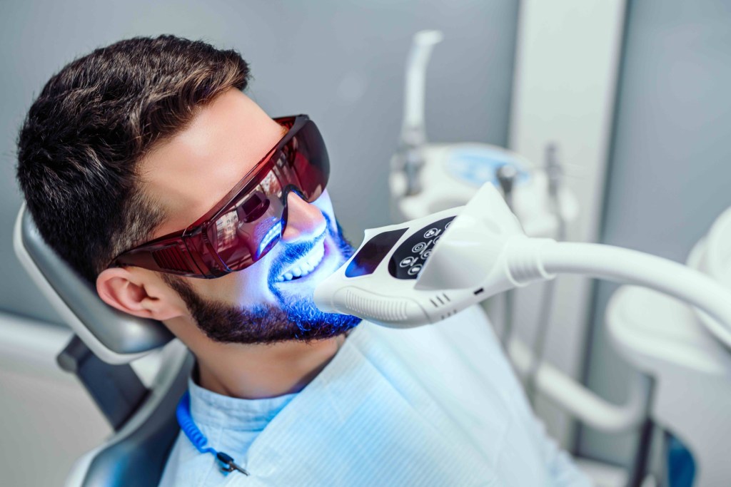 Man sitting in dentist office receiving teeth whitening treatment
